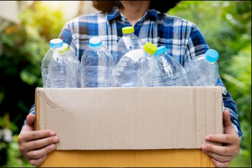 Mujer cargando botellas de plástico en una caja de cartón Mujer cargando botellas de plástico en una caja de cartón