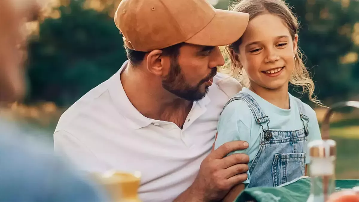 Adult and child sharing time outdoors during a family meal in a natural setting